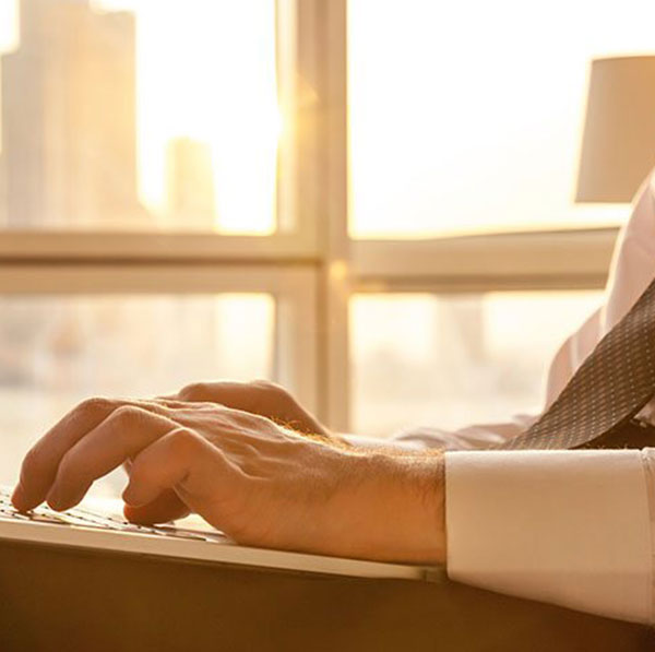 A business man dressed in a brown tie typing on a thin white laptop.