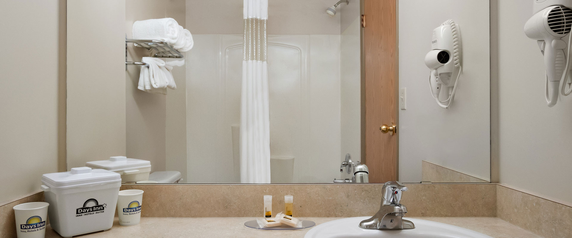 Large view of a guest bathroom at Days Inn Red Deer, Alberta with large mirror over the sink and a shower and shower curtain.
