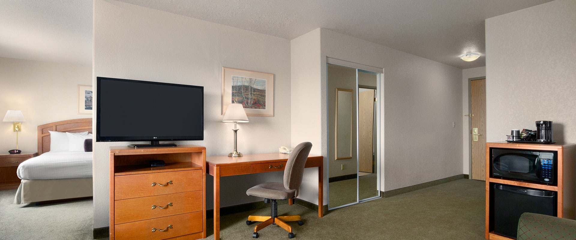 Large view of a suite at Days Inn Red Deer, Alberta with a rectangular work table and chair, a TV perched on a cabinet of drawers and mirrored closet.
