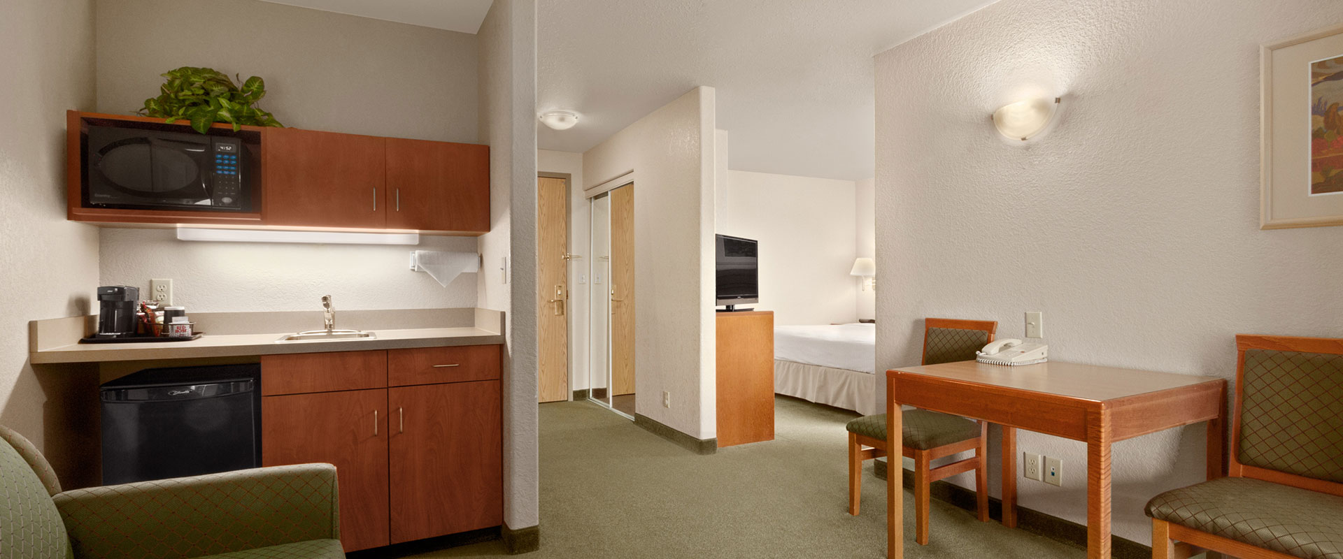 Large view of a compact kitchenette suite with microwave, dishwasher and square table with seating at Days Inn Red Deer, Alberta.
