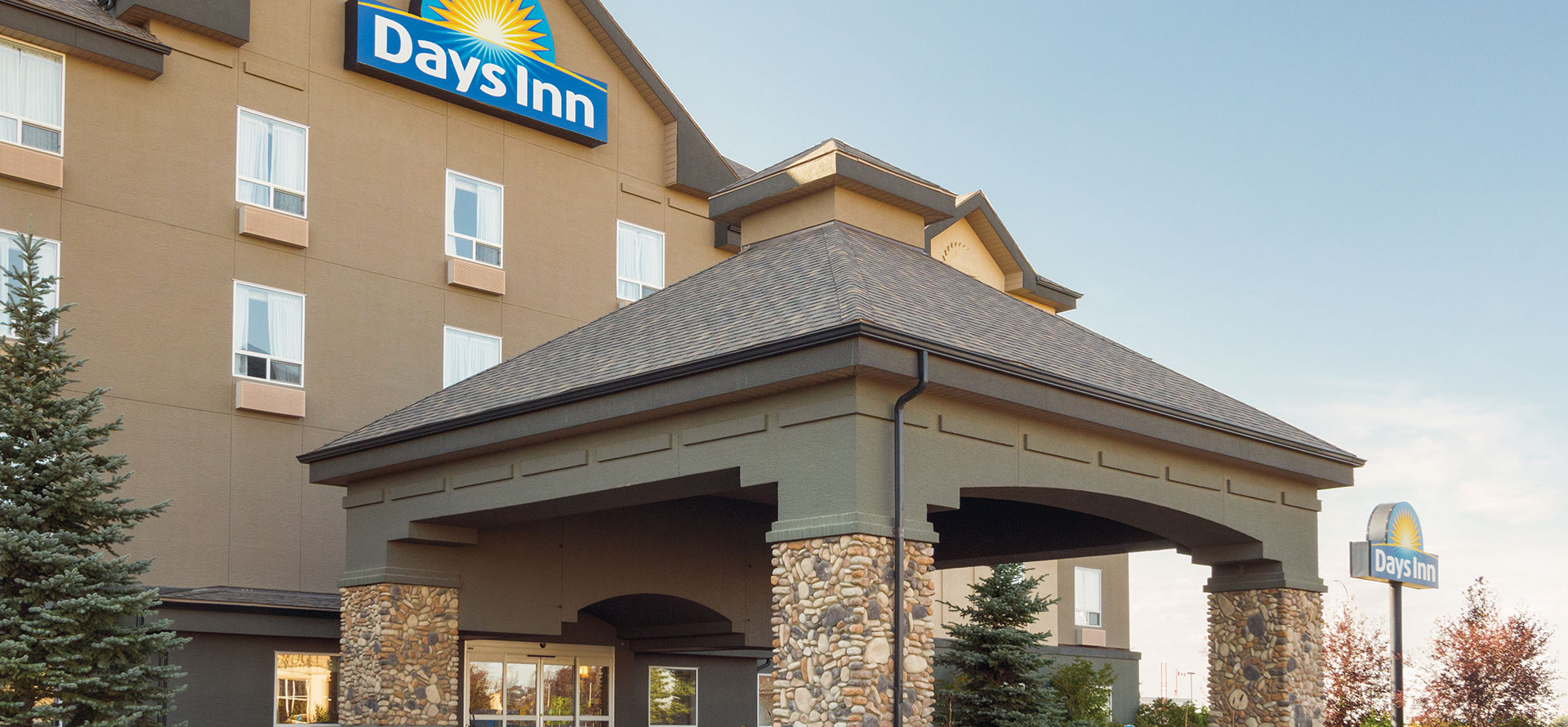 Large view of the portico covered entranceway, flanked by pine trees to Days Inn Red Deer, Alberta.
