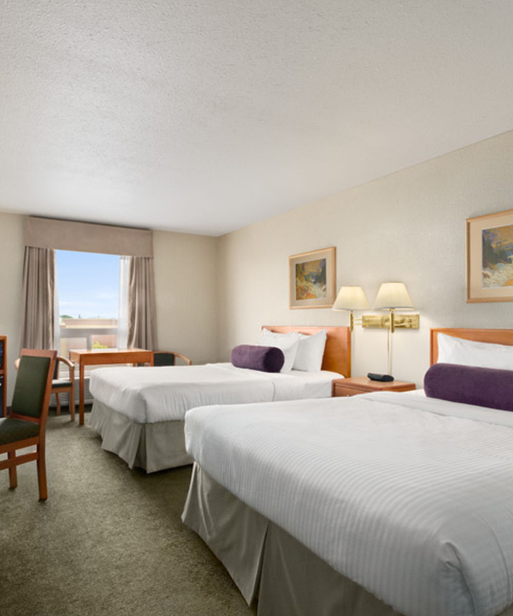 Two bed suite at Days Inn Red Deer, Alberta with a large window draped with beige curtains, sitting chairs and a rectangular table.
