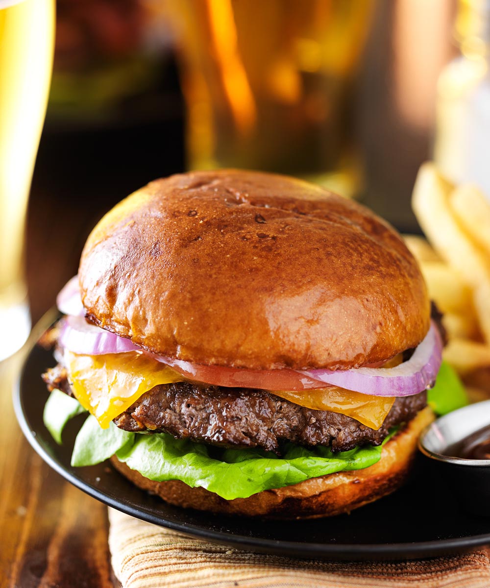 Large image of a hamburger with onions, tomatoes and lettuce served on a platter.