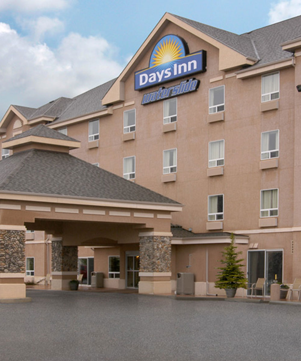 Part view of the main entrance to Days Inn Red Deer, Alberta featuring a large stone and concrete portico and the corporate at the the top of the hotel.
