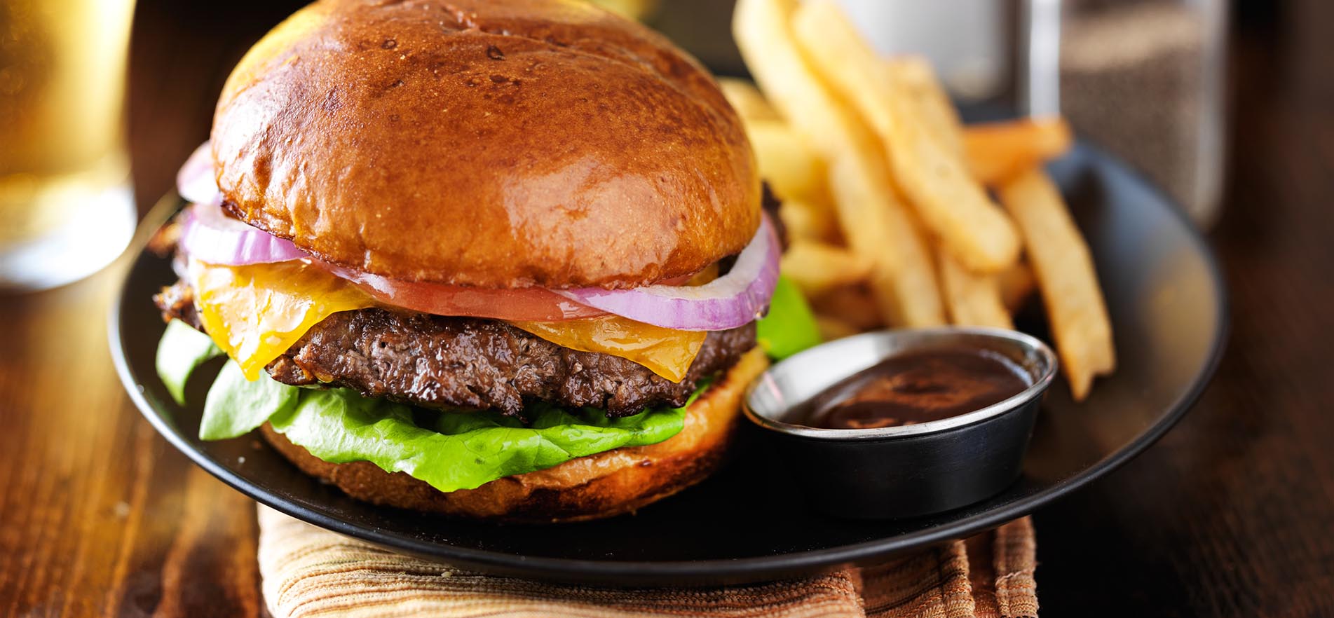 Large image of a hamburger with onions, tomatoes and lettuce served with fries and gravy.