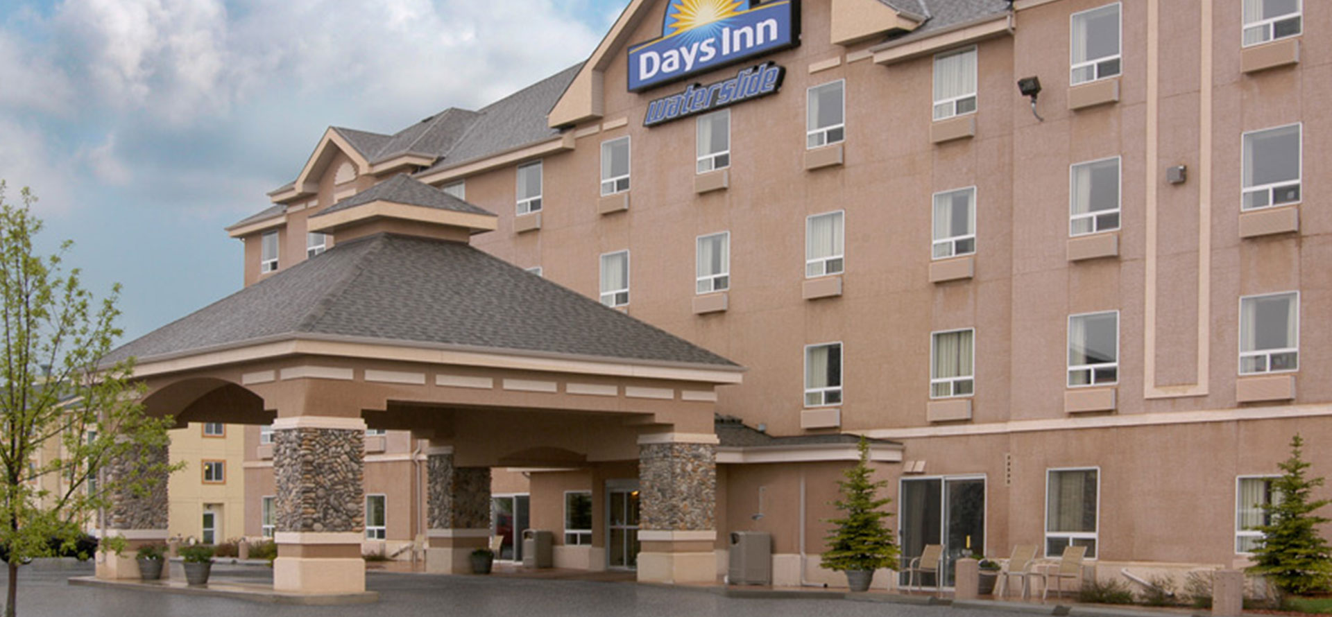 Large view of main entrance to Days Inn Red Deer, Alberta with a stone and concrete portico and the corporate logo placed at the summit of the hotel.
