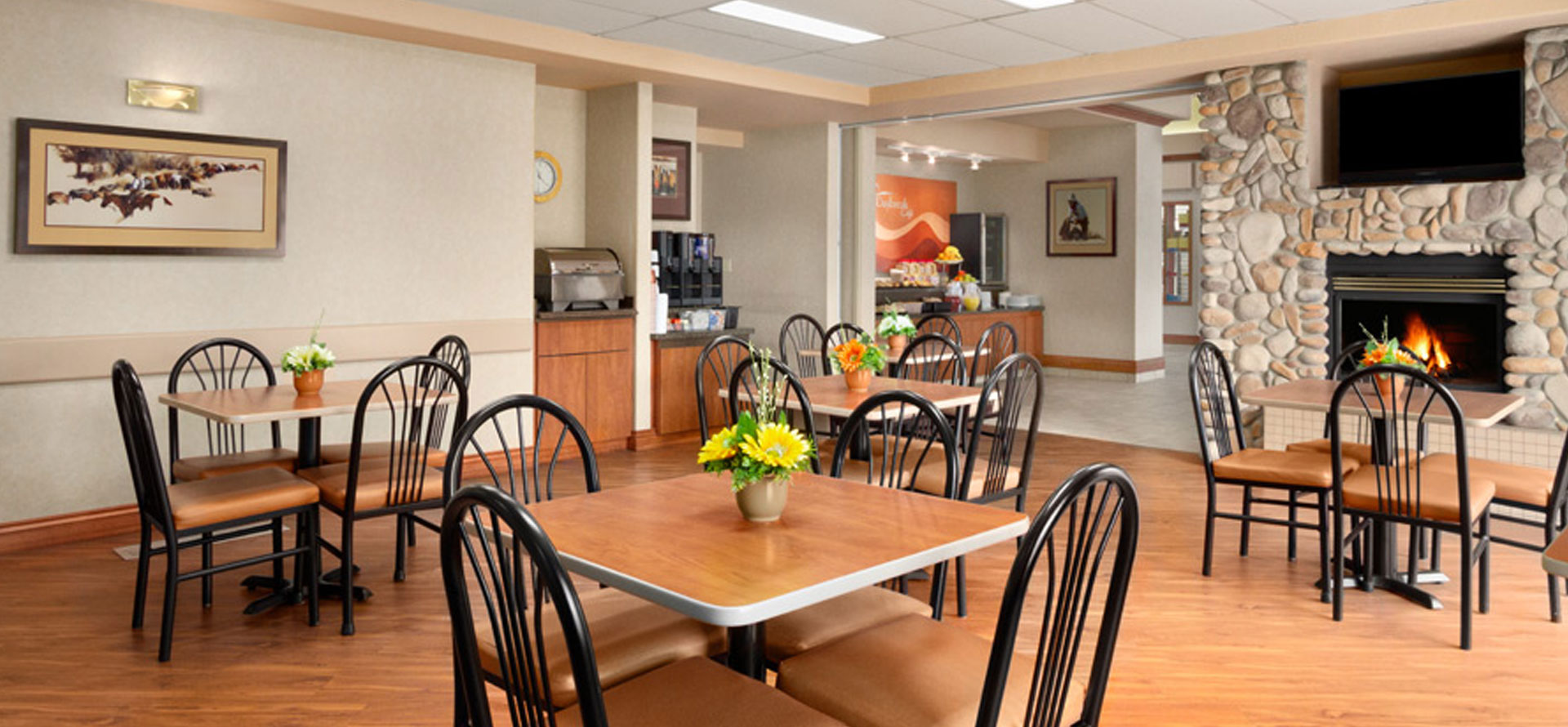 Large view of the sunny breakfast room at Days Inn Red Deer, Alberta with tables and bright fresh flowers and roaring fireplace.
